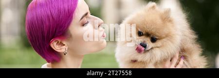 femme aux cheveux violets bougeant les lèvres et tenant le drôle pomeranian spitz sortant de la langue, bannière Banque D'Images