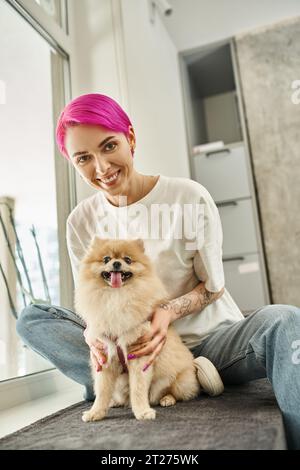 chien sitter heureux et élégant serrant spitz pomeranian moelleux et regardant la caméra dans l'hôtel pour animaux de compagnie Banque D'Images