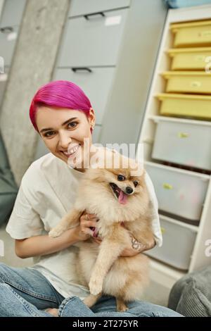 chien sitter aux cheveux violets souriant câlinant spitz pomeranian et regardant la caméra dans l'hôtel pour animaux de compagnie Banque D'Images