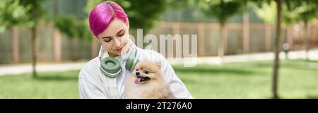 propriétaire d'animal de compagnie femelle avec les cheveux violets et écouteurs tenant mignon pomeranian spitz dans les mains, bannière Banque D'Images