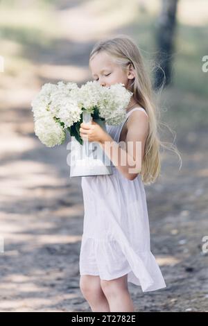 Portrait d'une jeune belle fille tenant un bouquet d'hortensias blanches dans ses mains. Regarde les fleurs. Cadre vertical. Banque D'Images