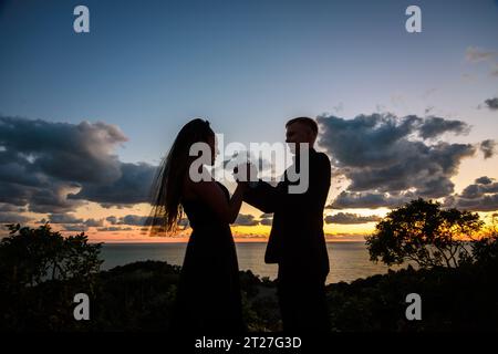 Heureux jeune couple tenant les mains de l'autre dans le rétro-éclairage sur fond de coucher de soleil Banque D'Images