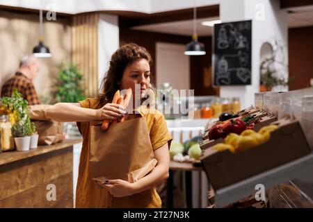 Acheteur respectueux de l'environnement achetant des produits alimentaires écologiques dans un magasin zéro déchet en utilisant des sacs en papier pour minimiser l'utilisation de plastique. Client vivant vert à la recherche de légumes sains sans produits chimiques Banque D'Images