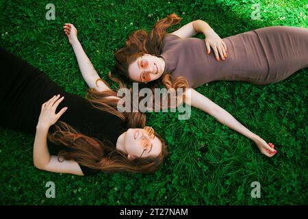 Young Cute Twins Sisters allongés sur un fond de pelouse verte en plein air Banque D'Images