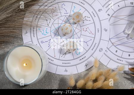Roue du zodiaque, thème natal, bougie allumée et dés d'astrologie sur table grise, mise à plat Banque D'Images