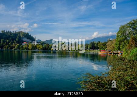 Vue sur le lac de Bled avec des bateaux pletna amarrés, des bateaux traditionnels fabriqués à la main par les habitants de Bled et l'église de St. Martin, à Bled, Alpes slovènes, SL Banque D'Images