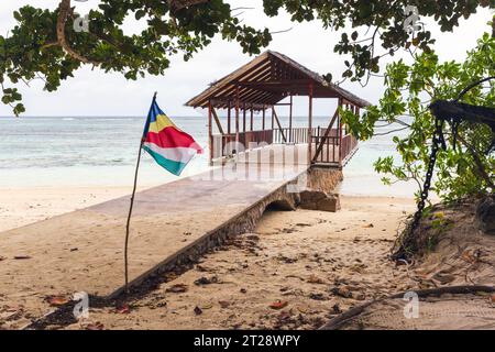 Plage d'Anse Union, île de la Digue, Seychelles. Paysage avec drapeau et un gazebo vide à la vieille jetée sur un fond Banque D'Images