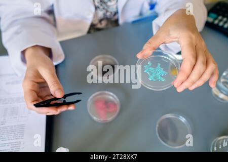 Femme scientifique méconnaissable montrant des paillettes bleues dans un échantillon de crème pour le visage sur une boîte de Pétri au labo Banque D'Images