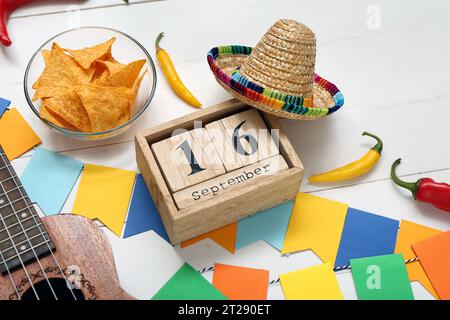 Calendrier cube avec date SEPTEMBRE 16, nachos, piments et sombrero sur fond en bois blanc. Célébration du jour de l'indépendance du Mexique Banque D'Images