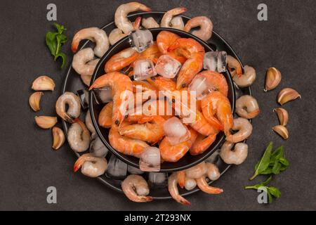 Crevettes tigrées et crevettes dans la plaque noire avec de la glace. Fond noir. Alimentation saine. Vue à plat Banque D'Images