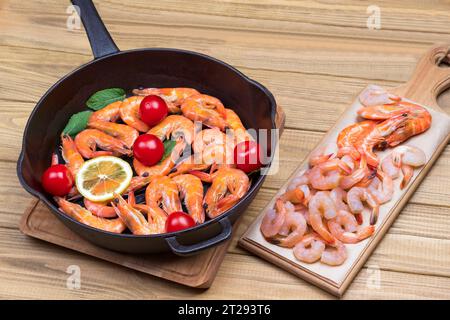 Crevettes tigrées crevettes avec tomates et citron dans une poêle. Crevettes sur planche à découper. Fond en bois clair. Nourriture saine et appétissante. Vue de dessus Banque D'Images