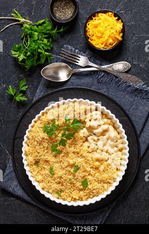 gros plan mac cuit et fromage saupoudré de chapelure panko et de persil frais dans un plat allant au four sur une table en béton, vue verticale, pose à plat Banque D'Images