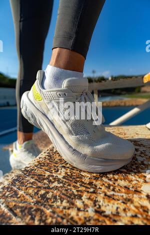 Gros plan des chaussures de course blanches d'une femme sportive escaladant des escaliers en fer rouillé pour renforcer les fessiers et les quadriceps par une journée ensoleillée Banque D'Images