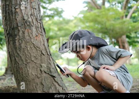 Garçon asiatique portant un chapeau dans une combinaison d'exploration forestière utilisez une loupe pour surveiller la zone des arbres. Banque D'Images