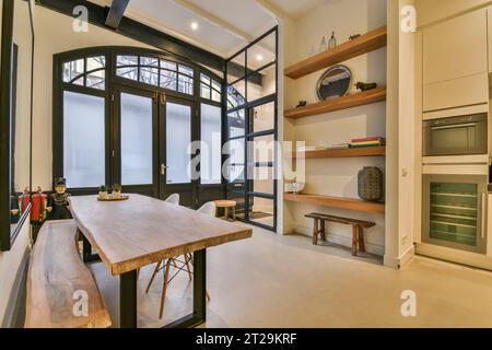 Intérieur de cuisine moderne avec décors sur étagères et table en bois avec banc arrangé par de grandes portes fermées à la maison Banque D'Images