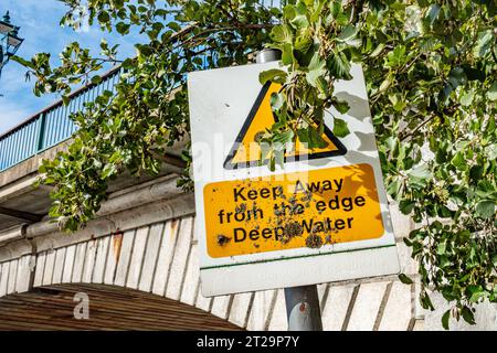 Un panneau de Staines Bridge avertissant du danger des eaux profondes est partiellement masqué par une branche d'arbre Banque D'Images