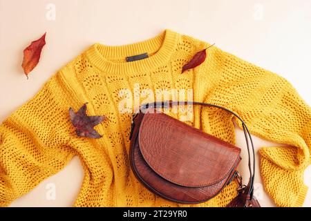 Pose à plat du pull jaune de la femme et sac brun, feuilles d'automne sur fond beige. Concept de mode d'automne. Vue de dessus, pose à plat. Banque D'Images