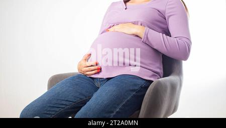 Fille enceinte assise sur une chaise au lieu de travail, fond blanc. La notion de congé de maternité et le paiement des prestations sur le lieu de travail. Banque D'Images