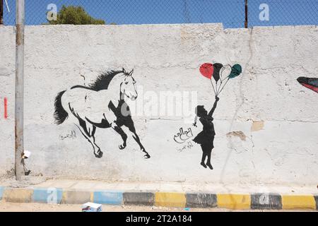 Dhiban Jordan Street art dans le style de Banksy sur un mur dans la petite ville de Dhiban comprenant une fille avec des ballons et un cheval vu en août 2023 Banque D'Images