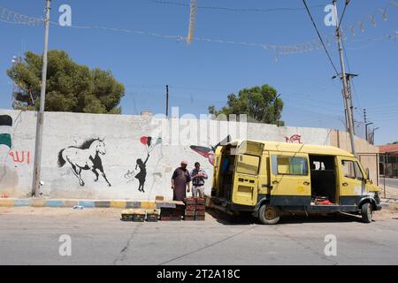 Dhiban Jordan Street art dans le style de Banksy sur un mur dans la petite ville de Dhiban aux côtés du vendeur de fruits et légumes vu en août 2023 Banque D'Images