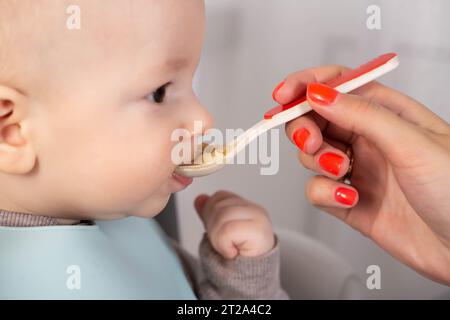 La première alimentation avec de la purée de fruits pour un bébé garçon de 6 mois. Banque D'Images