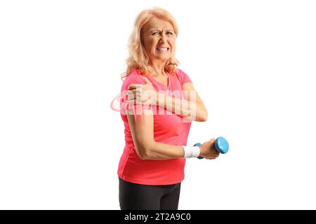 Femme en sportswear avec épaule douloureuse tenant un haltère et regardant la caméra isolée sur fond blanc Banque D'Images