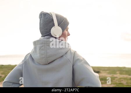 Femme portant des écouteurs et chapeau de laine écoutant de la musique et profitant de la vue à l'extérieur. Concept de style de vie hivernal. Banque D'Images