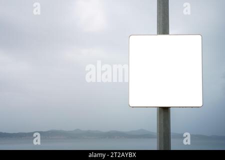 Gros plan du panneau blanc vide à côté de la mer le jour couvert. Banque D'Images