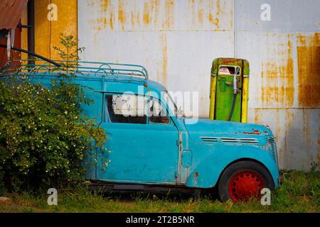 Vue d'une vieille voiture américaine bleue avec des roues rouges garées près d'une vieille pompe à essence Banque D'Images