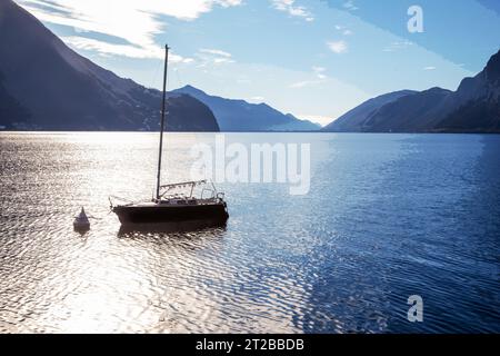 Superbe paysage ensoleillé avec un voilier d'abri ancré dans l'eau sur le lac de Lugano et les Alpes suisses de l'autre côté du lac de Lugano Banque D'Images