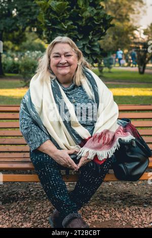 Portrait d'une femme âgée joyeuse se relaxant à l'extérieur, assis sur un banc dans un parc public Banque D'Images