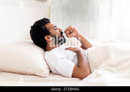 Malade jeune Indien toussant alors qu'il est allongé dans le lit à la maison Banque D'Images