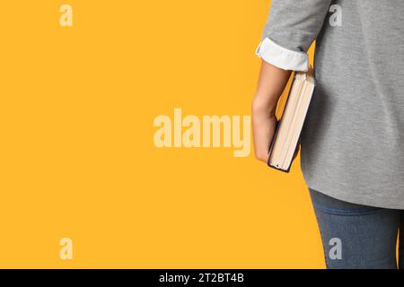 Belle jeune femme asiatique avec Bible sur fond jaune, vue arrière Banque D'Images