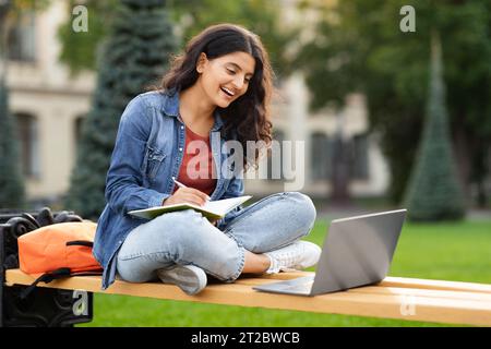 Jeune étudiante hindoue avec ordinateur portable et Notepad étudier à l'extérieur Banque D'Images