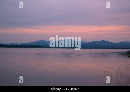 Coucher de soleil dans le réservoir Gabriel y Galan avec des montagnes en arrière-plan et de l'eau soyeuse Banque D'Images