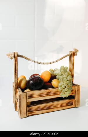 Il y a des fruits dans un panier sur une table blanche - prunes, abricots et raisins. Cadre vertical Banque D'Images