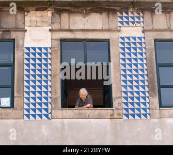 Femme portugaise âgée à la fenêtre avec des carreaux azulejo traditionnels bleus et blancs à Porto Banque D'Images
