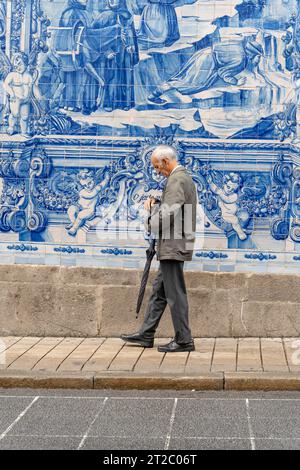 Homme âgé passant devant les carreaux Capela das Almas Azulejo à Porto, Portugal Banque D'Images