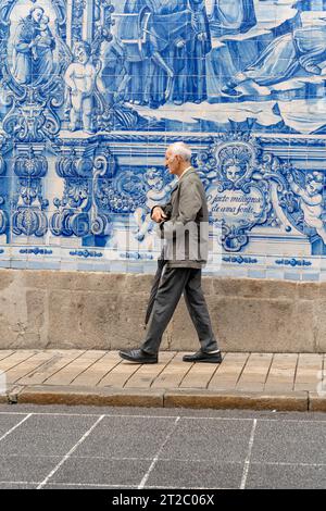 Homme âgé passant devant les carreaux Capela das Almas Azulejo à Porto, Portugal Banque D'Images