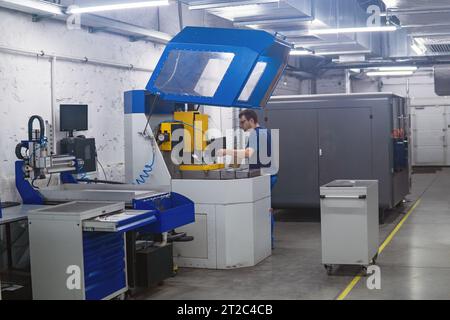 Perm, Russie - 13 juillet 2023 : travailleur dans l'atelier régule le fonctionnement d'une machine à travailler les métaux Banque D'Images