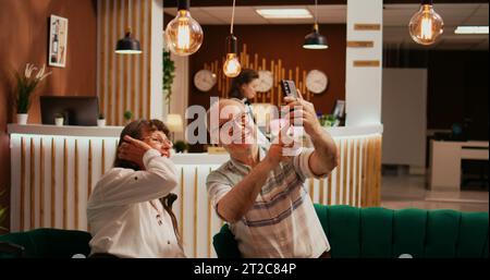 Personnes âgées prenant des photos dans le hall, enregistrant toutes les activités pendant les vacances de retraite à l'étranger. Vieux mari et femme prennent des photos sur smartphone, faisant des souvenirs pour les membres de la famille. Banque D'Images
