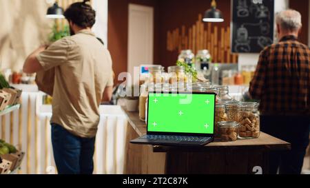 Ordinateur portable Chroma Key avec espace de copie utilisé comme signe commercial dans un magasin local utilisant de l'énergie renouvelable. Publicité promotionnelle sur dispositif à écran vert dans un magasin d'alimentation avec des produits dans des contenants métalliques réutilisables Banque D'Images