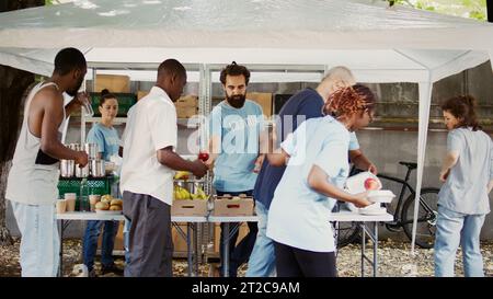 Lors de la collecte de nourriture humanitaire, un homme caucasien âgé avec des béquilles est aidé par une gentille femme noire. Les jeunes volontaires apportent une aide humanitaire aux pauvres, aux sans-abri et aux handicapés. Prise de vue à main levée. Banque D'Images