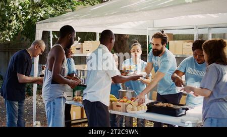 Les jeunes volontaires des communautés caucasienne et afro-américaine donnent gratuitement aux moins fortunés de la nourriture et des nécessités. Des volontaires offrant une aide humanitaire et un soulagement de la faim aux nécessiteux. Portable. Banque D'Images