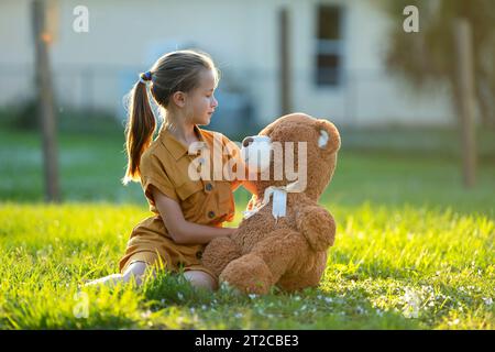 Une fille heureuse embrassant son ours en peluche à l'extérieur sur une pelouse en herbe verte. Concept d'amitié Banque D'Images