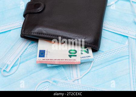 Portefeuille noir pour homme avec de l'argent en euros à l'intérieur sur les masques médicaux jetables bleus. Échange de masques médicaux. Affaires pendant une pandémie ou une épidémie Banque D'Images