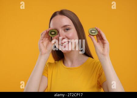 Jeune femme tenant des moitiés de kiwi sur fond jaune Banque D'Images