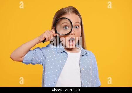 Mignon petite fille regardant à travers loupe sur fond jaune Banque D'Images