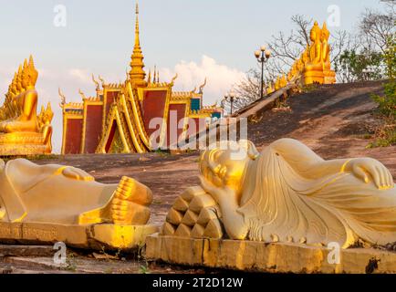 Rangées de belles, miniatures, sculptures d'or vibrantes de Bouddha, illuminées par le soleil couchant, alignées au sommet d'un mur en pente, à côté du temple, Banque D'Images