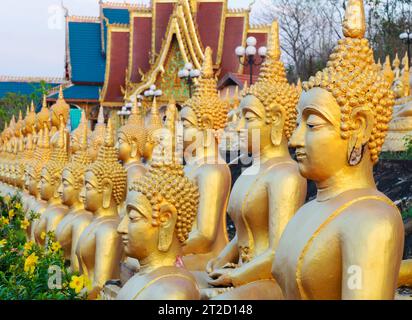 Rangées de belles, miniatures, sculptures d'or vibrantes de Bouddha, illuminées par le soleil couchant, alignées au sommet d'un mur en pente, à côté du temple, Banque D'Images